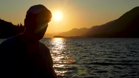 Sunset-on-a-lake-with-mountains-in-the-background-with-a-guy-checking-his-phone-in-Silhouette