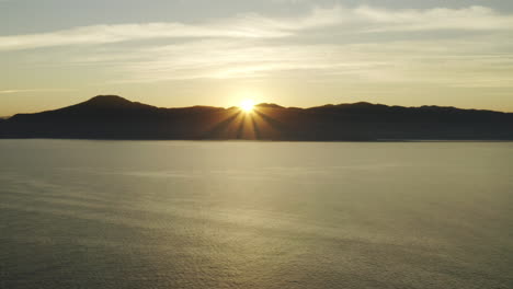 Wunderschöne-Luftdrohnenansicht-Des-Sonnenuntergangs-über-Dem-Meer-Und-Den-Bergen-Am-Horizont
