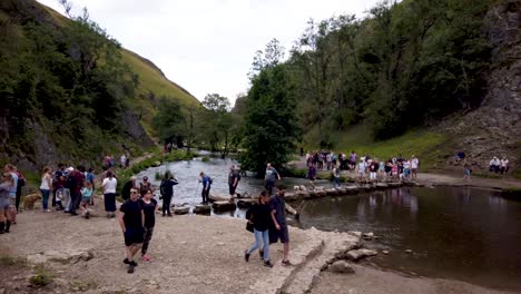 Dovedale-Stepping-Stones-in-Derbyshire,-Peak-District,-England,-UK-showing-crowds-of-tourists-crossing-the-stepping-stones-over-the-river-Dove