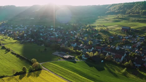 aerial-view-of-small-swiss-village-settlement-in-green-forest-covered-valley-in-canton-aargau-Switzerland,-spring-yellow-flowers,-village-church