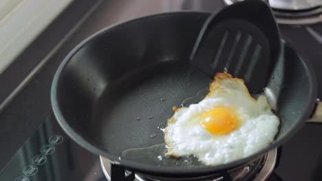 One-crispy-egg-frying-on-small-amount-of-sunflower-oil-in-a-black-pan-slighly-moved-by-a-black-plastic-spatula