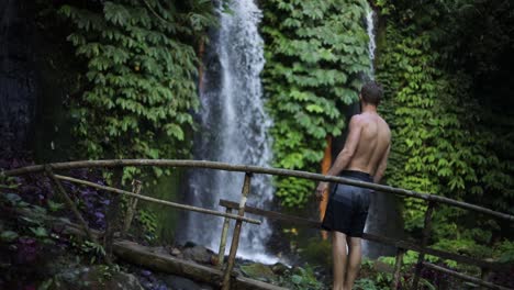 Toma-En-Cámara-Lenta-De-Un-Hombre-Caminando-Frente-A-Una-De-Las-Muchas-Hermosas-Cascadas-De-Banyu-Wana-Amertha-En-Las-Selvas-De-Bali,-Indonesia
