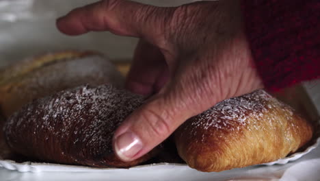 Close-up-hand-of-woman-with-age-spots-picking-up-a-traditional-famous-italian-neapolitan-pastry-called-sfogliatella-napoletana-4k