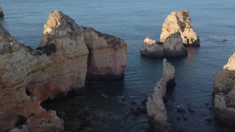 Golden-limestone-sea-cliffs-and-rock-stacks-along-Portuguese-coast-near-Lagos,-high-angle