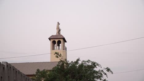 Church-steeple-and-statue-during-sunset-in-La-Molina,-Lima,-Peru-PAN-FROM-LEFT-TO-RIGHT