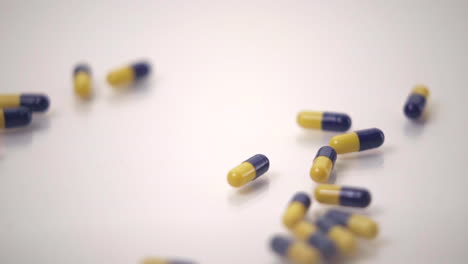 Zeitlupenmakro-Von-Blauen-Und-Gelben-Pillen,-Die-Eine-Gelbe-Pille-Aus-Dem-Rahmen-Auf-Weißem-Hintergrund-Schieben