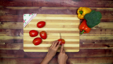 Eine-Draufsicht-Auf-Das-Schneiden-Der-Tomaten-Von-Hand,-Zwei-Große-Gelbe-Und-Rote-Paprika-Und-Ein-Grüner-Brokkoli-Auf-Dem-Tisch