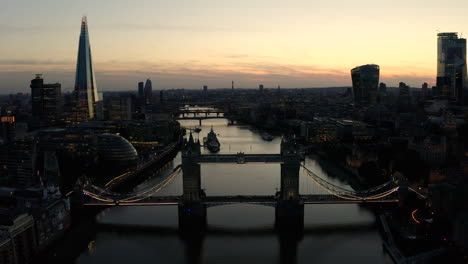 Aerial-view-of-London,-River-Thames,-and-Tower-Bridge-just-after-the-sun-has-set-and-the-sky-is-lit