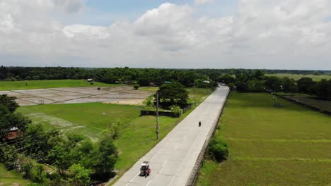 Aerial-shot-of-a-two-lane-highway-with-minimal-traffic-in-the-province-of-Malasiqui,-Pangasinan,-Philippines-surrounded-by-huge-farm-fields