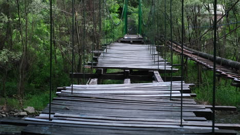 Old-damaged-wooden-bridge-with-missing-laths-over-a-river-in-the-forest