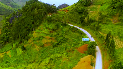 Aerial-dolly-forward-of-a-winding-road-cut-into-the-mountainside-of-the-misty-mountains-of-the-Dong-Van-Karst-plateau-geopark