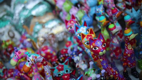 Slow-Motion-handheld-shot-of-a-collection-of-Asian-"Beckoning-Cat"-dolls-at-an-outdoor-public-street-market-in-Bali,-Indonesia