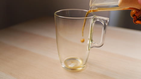 Pouring-coffee-from-a-glass-french-press-with-a-wooden-handle-when-viewed-from-below-on-a-tall-glass-caught-by-pouring-coffee-and-bubbles-on-the-side-in-slow-motion-capture-at-120-FPS