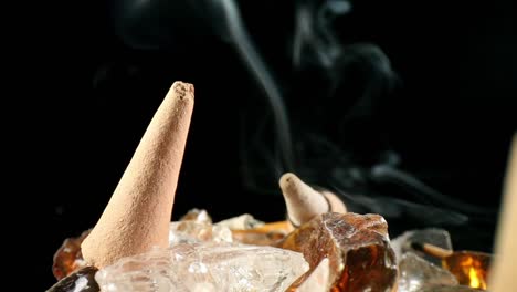 Close-up-of-unlit-incense-cone-in-a-decorative-rock-garden,-a-lit-cone-w--smoke-billowing-in-off-focus