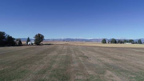 A-zoom-out-along-a-corn-field-with-a-farmhouse-backed-by-majestic-mountains