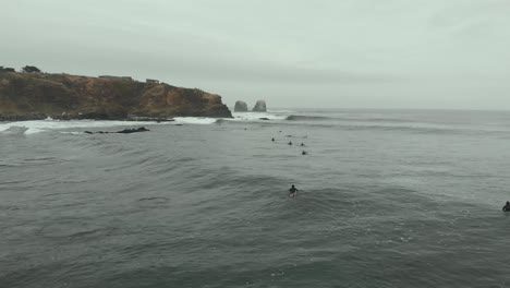 Aerial-Drone-shot-going-forward-over-Surfers-on-a-cold-day-at-the-sea,-Pichilemu,-Chile-4K