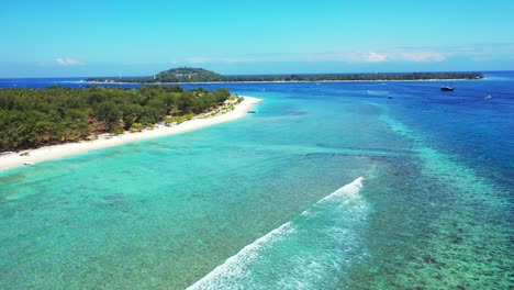 White-waves-splashing-on-great-coral-reef-and-rocky-seabed-on-seashore-of-tropical-island-with-lush-vegetation-and-white-beach-in-Indonesia