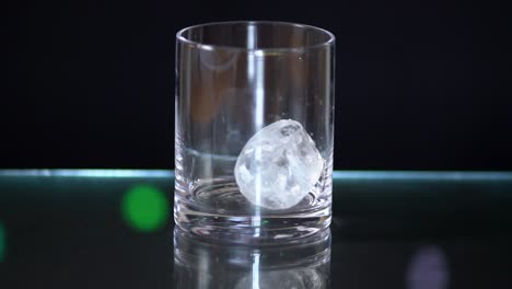 Giant-Ice-cubes-falling-into-a-liquor-glass-sitting-on-top-of-a-glass-surface-with-a-black-background-with-fairy-lights