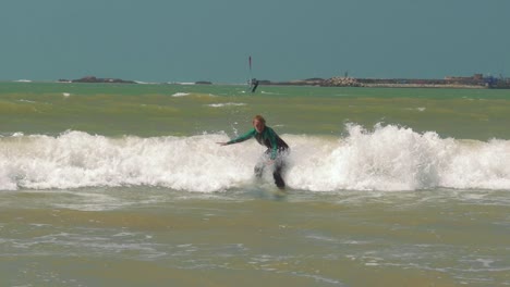 Beginner-surfer-girl-falling-off-surfboard-into-waves,-Morocco,-Essaoiura