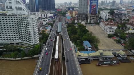 Bangkok,-Tailandia---Skytrain-Corriendo-En-El-Ferrocarril-Sobre-El-Río-Chao-Phraya-Junto-Con-Otros-Vehículos-En-El-Puente-Saphan-Taksin---Toma-Aérea-De-Drones