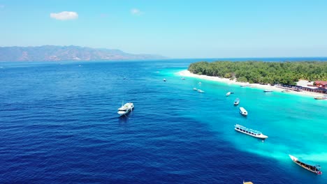 Touring-boats-anchored-on-blue-azure-lagoon-near-resort-located-on-tropical-island-shore-with-white-sandy-beach-and-trees-forest-in-Bali
