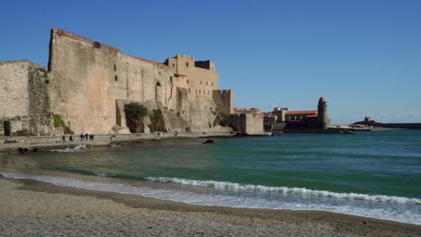 The-beach,-fortress-and-old-town-of-Collioure-during-high-winds-on-a-bright-hot-day