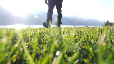 Male-Hiker-Walking-Towards-Camera-On-Grass-Beside-Lake-In-Walenstadt,-Switzerland