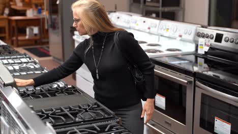 Closeup-of-pretty-mature-blonde-woman-looking-at-the-features-and-benefits-of-a-gas-stove-in-a-kitchen-appliance-store