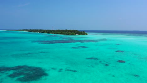 Quiet-tropical-island-with-lush-vegetation-and-palm-trees-in-the-middle-of-Indian-ocean,-surrounded-by-calm-lagoon-with-coral-reef-on-seabed