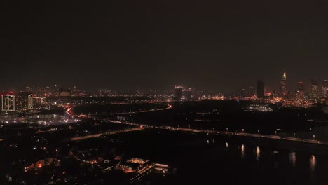 Eiree-descending-drone-shot-over-Saigon-river-in-Ho-Chi-Minh-City,-Vietnam-at-night-showing-the-city-skyline-and-bridge-to-District-two