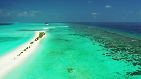 Long-white-sandy-beach-surrounded-by-turquoise-calm-water-of-shallow-lagoon-and-coral-reefs-barrier-in-the-middle-of-deep-blue-ocean,-Maldives