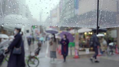 View-While-Holding-A-Clear-Wet-Umbrella-On-A-Rainy-Day-In-Tokyo,-Japan-With-People-In-The-Blurry-Background---Closeup-Shot