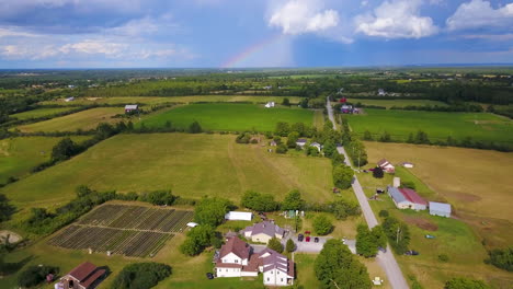 Aerial-rise-over-a-farm-with-a-rainbow-and-storm-clouds-in-the-distance