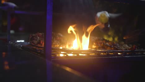 Gloved-Hands-Turning-Roasted-Chicken-Over-A-Fire-Grill-At-Night,-Medium-Close-Up