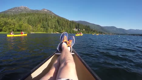 Slow-motion-POV-point-of-view-shot-as-a-man-resting-legs-on-a-boat,-people-canoeing-on-a-lake