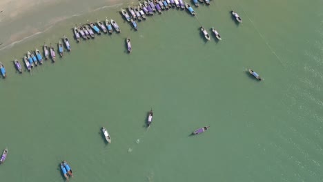Top-down-drone-shot-of-longtail-boats-floating-in-the-water-next-to-the-beach-in-Ao-Nang-Thailand