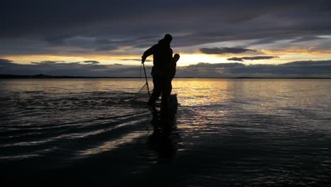 Männer-Angeln-Im-Seichten-Wasser-In-Neuseeland-Mit-Dem-Wunderschönen-Orangefarbenen-Sonnenuntergang-Im-Hintergrund---Zeitlupe