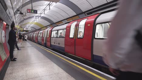 London-underground-train-full-of-people-leaving-subway-platform,-crowd-of-people-passing-camera
