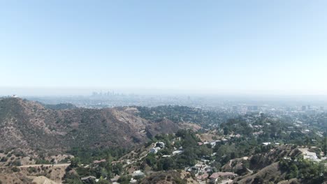 A-high-altitude-forward-moving-aerial-over-Hollywood-hill-overseeing-a-hazy-landscape-with-Los-Angeles-in-the-far-distance
