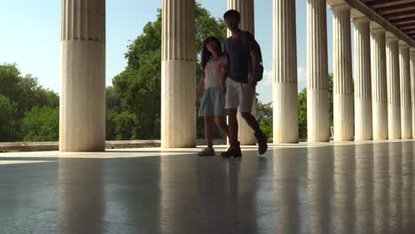 sweet-asian-couple-walking-at-isle-of-greek-pillars,-still-ground-level