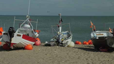 Barcos-De-Pescadores-Con-Banderas-Ondeantes-En-La-Playa-Con-Agua-En-El-Fondo,-Toma-Panorámica-Media