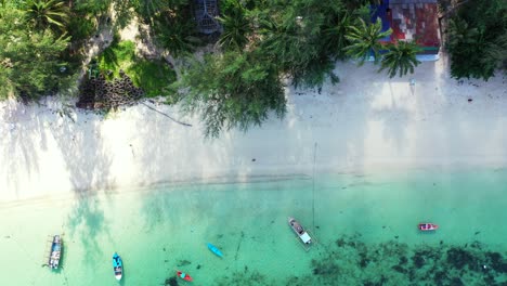 Wunderschöner-Weißer-Sandstrand-Mit-Palmen,-Umspült-Von-Türkisfarbener-Lagune,-Verankerte-Boote-Am-Ufer-Einer-Tropischen-Insel-In-Thailand