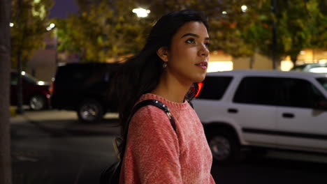 A-young-hispanic-woman-walking-and-shopping-at-stores-on-an-urban-city-road-under-street-lights-at-night