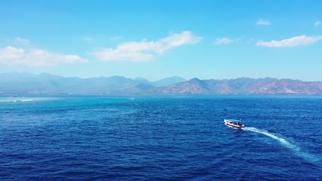 Barco-Navegando-A-Través-Del-Mar-Azul-Profundo-Hacia-La-Costa-De-La-Isla-Tropical-De-Montaña-En-Un-Cielo-Brillante-Con-Fondo-De-Nubes-Estáticas-Blancas,-Bali