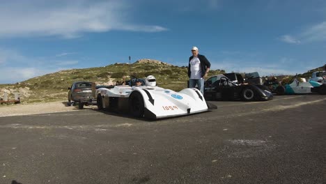 Man-Talking-To-The-Racer-Sitting-In-His-White-Racing-Car-With-Helmet-Off-At-The-Hill-In-Imtahleb-Malta--GoPro-Tilt-Pan-Shot
