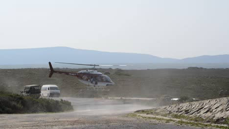 A-helicopter-takes-off-and-banks-creating-a-dust-cloud-in-a-rural-setting