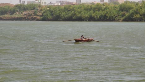 Man-rowing-a-small-fishing-boat-across-the-Nile-River-near-Khartoum,-Sudan