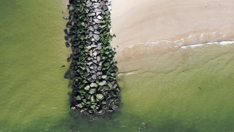 A-top-down-drone-view-of-a-stone-jetty-as-the-ocean-waves-gently-crash-onto-the-shore
