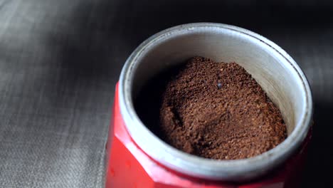 Zeitlupe-Eines-Aluminiumlöffels,-Der-Das-Mittlere-Fach-Einer-Roten-Italienischen-Kaffeemaschine-Mit-Kaffeepulver-Füllt-Und-Es-Gleichzeitig-Nivelliert