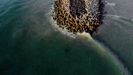 4k-Aerial-Fly-Backward-Reveal-Shot-of-a-Pier-with-waves-crashing-in-the-early-morning-during-sunrise-captured-with-a-drone,-Pondicherry,-India